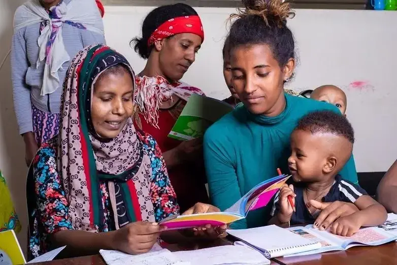 Women and small children look at notebooks and schoolbooks.