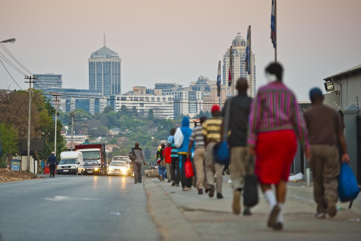 Viele Menschen laufen auf dem Gehweg neben einer Straße in Johannesburg, Südafrika.