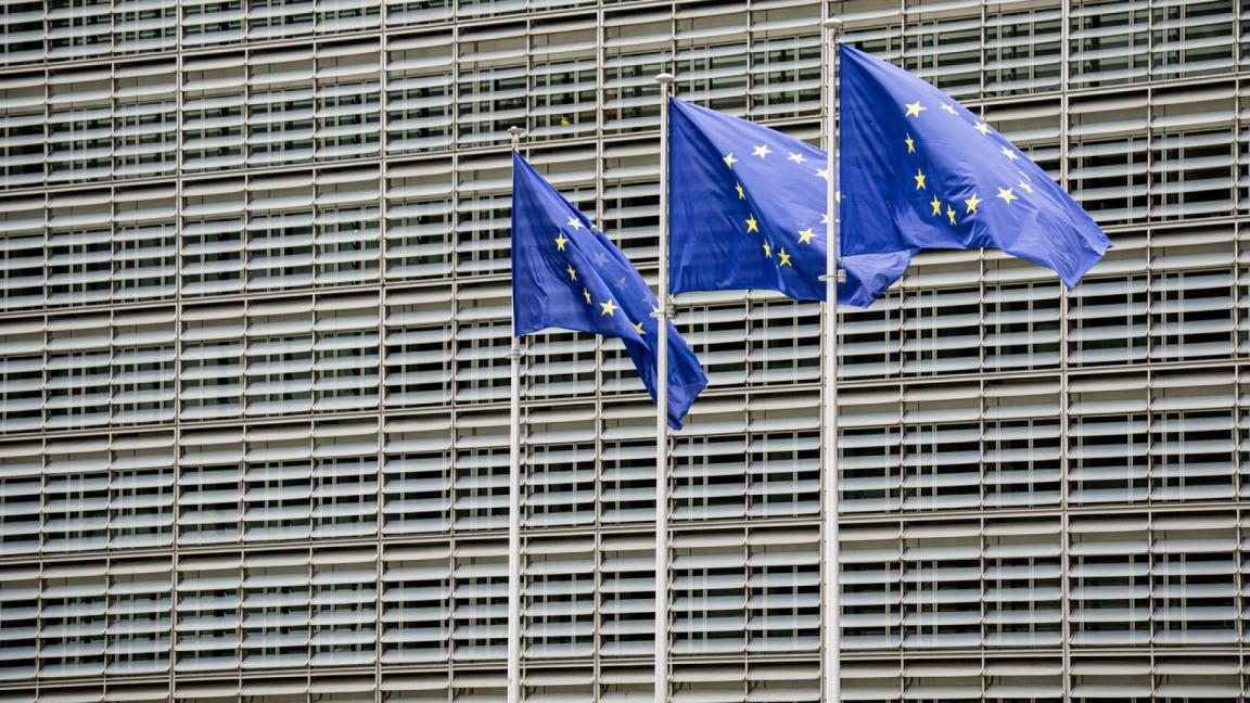 Three European Union flags waving in front of the Berlaymont building, the headquarters of the European Commission in Brussels.