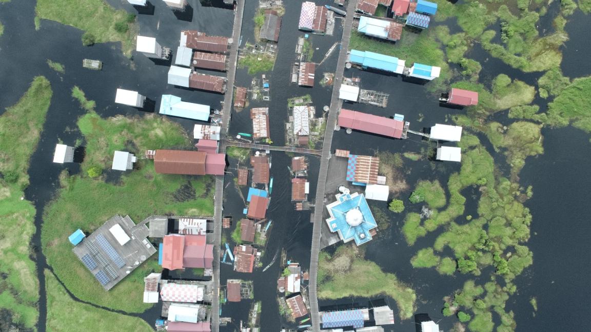 Aerial view of a flooded village in Indonesia with houses and roads surrounded by water and vegetation.