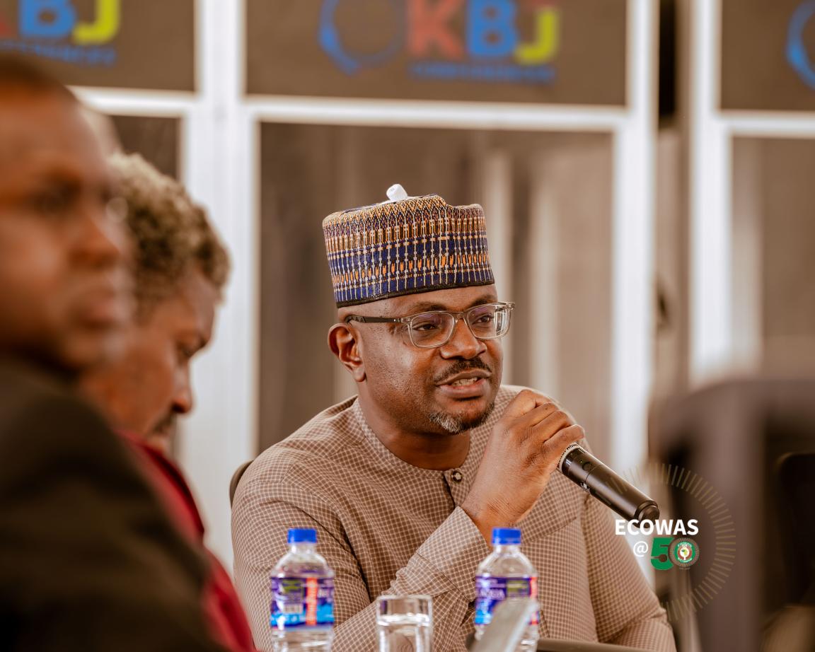 Une personne portant un chapeau et des lunettes parle dans un micro.