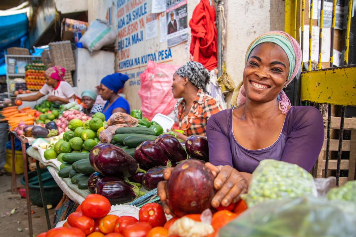 A woman selling vegetables stands behind a market stall.