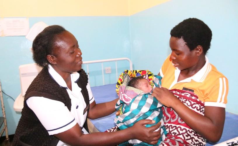 A nurse explaining to a mother holding her newborn how she can care for the baby.