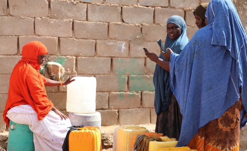 Women collecting water at a kiosk in an internally displaced persons (IDPs) camp in Somalia, with jerry cans placed nearby.