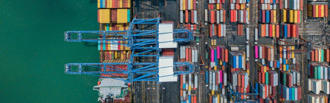 Vue aérienne d'un port à conteneurs avec de nombreux conteneurs colorés et des grues bleues.