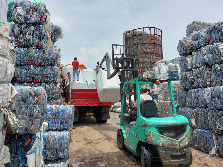 A forklift and a lorry with stacks of plastic bottles.
