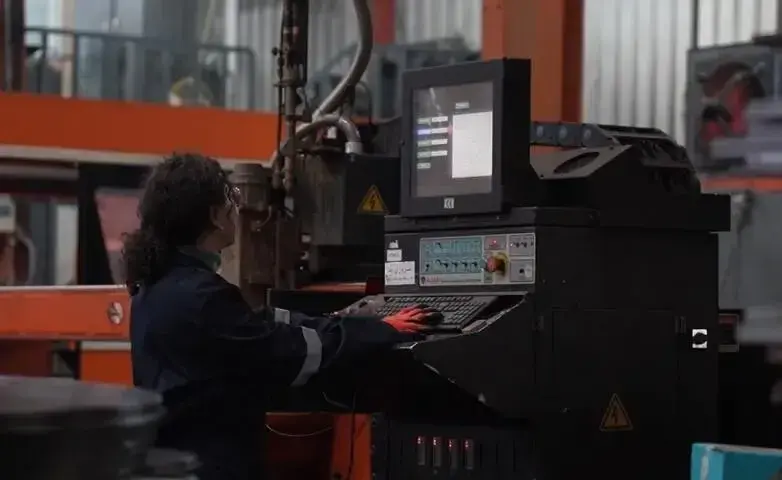 A woman in protective clothing works on a complex technical machine.