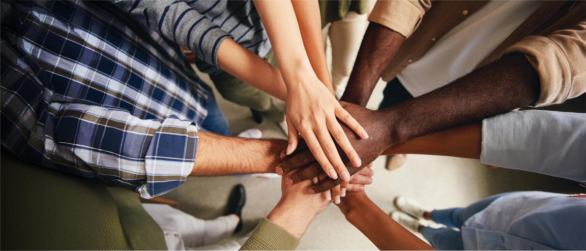 Several hands lie on top of each other in the centre of a circle.