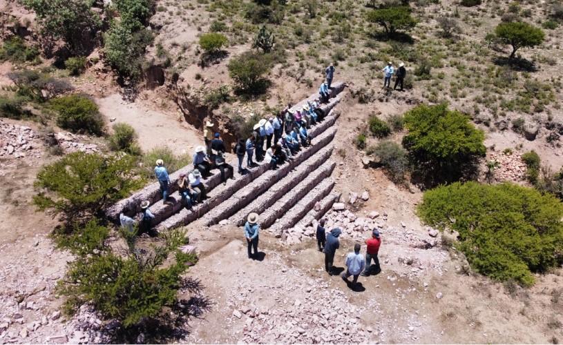 A group of people standing on stone terraces in a semi-arid landscape, observing erosion control measures.