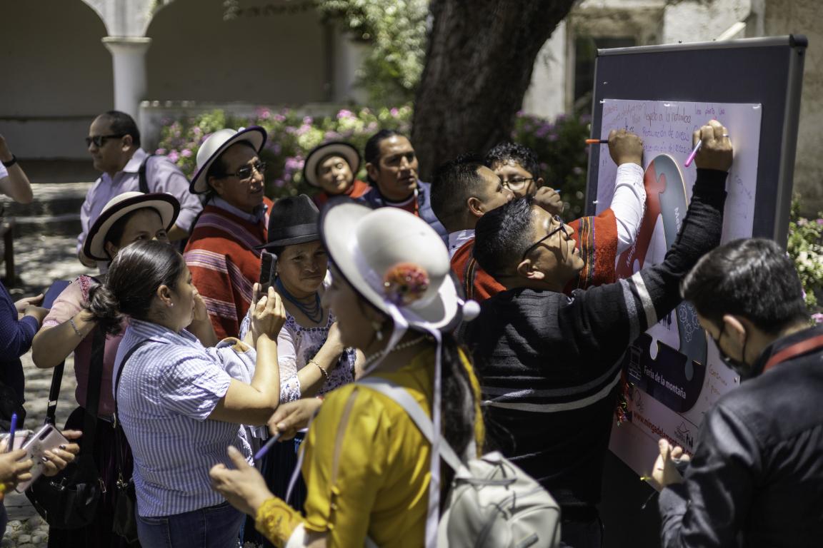 Gruppe von Menschen, die im Freien an einer Tafel schreiben und Fotos machen, umgeben von Bäumen und Säulen.