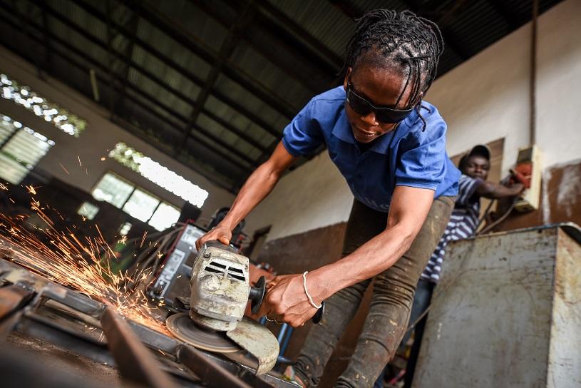 A female student uses a grinder to remove irregularities from an iron gate.