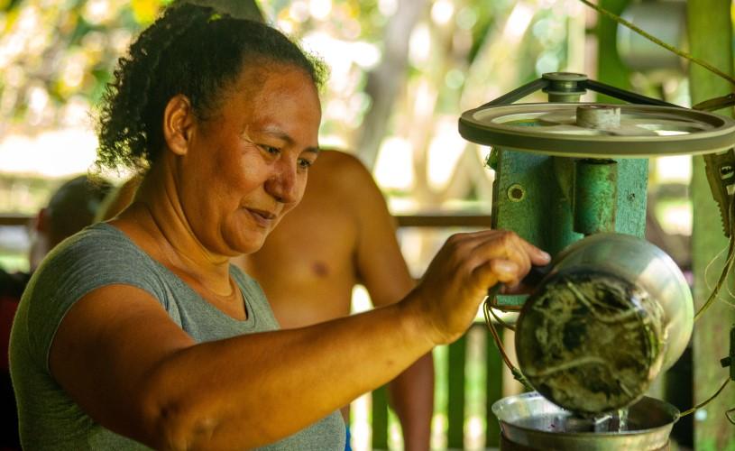 Uma mulher operando uma prensa para extrair polpa de açaí, uma importante fonte de renda para as mulheres na Amazônia rural 