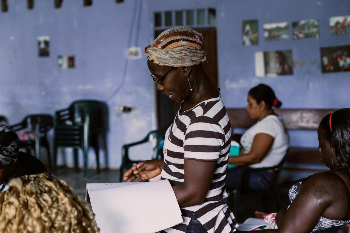 Eine schwarze Frau steht in einem Raum mit anderen schwarzen Frauen und trägt etwas vor.