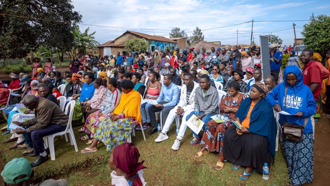 At a planning meeting in a Rwandan city, people sit together in rows outdoors.