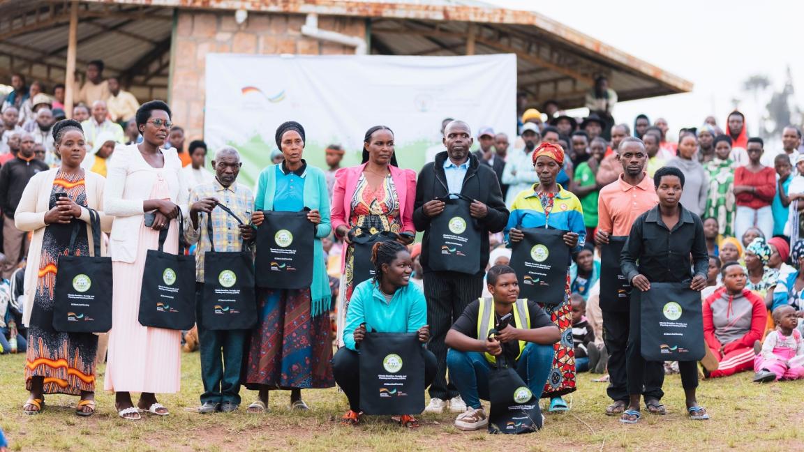 At a planning meeting in a Rwandan city, people sit together in rows outdoors.
