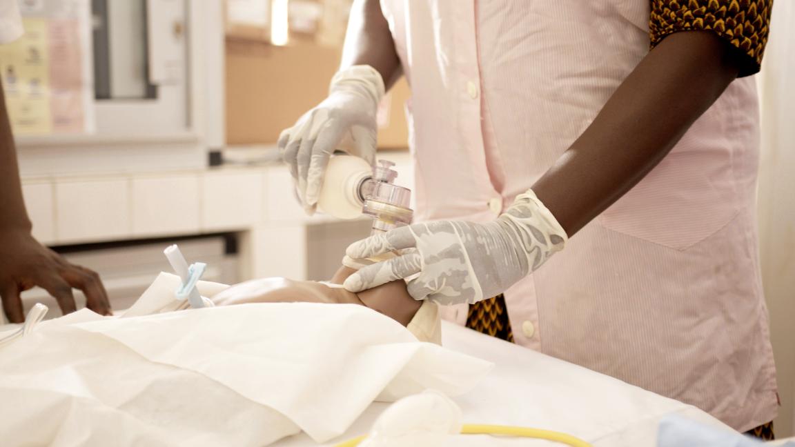 Person mit Handschuhen legt einen intravenösen Zugang an den Arm einer liegenden Person.