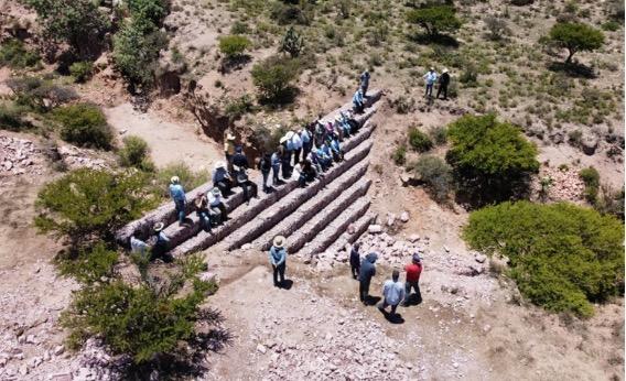 Eine Gruppe von Personen steht in einer semiariden Landschaft auf Steinterrassen und beobachtet Erosionsschutzmaßnahmen.