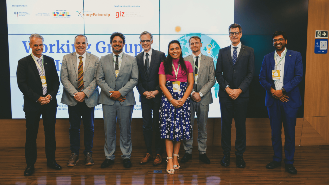 Seven men and a woman in business clothing smile and pose for a group photo. 