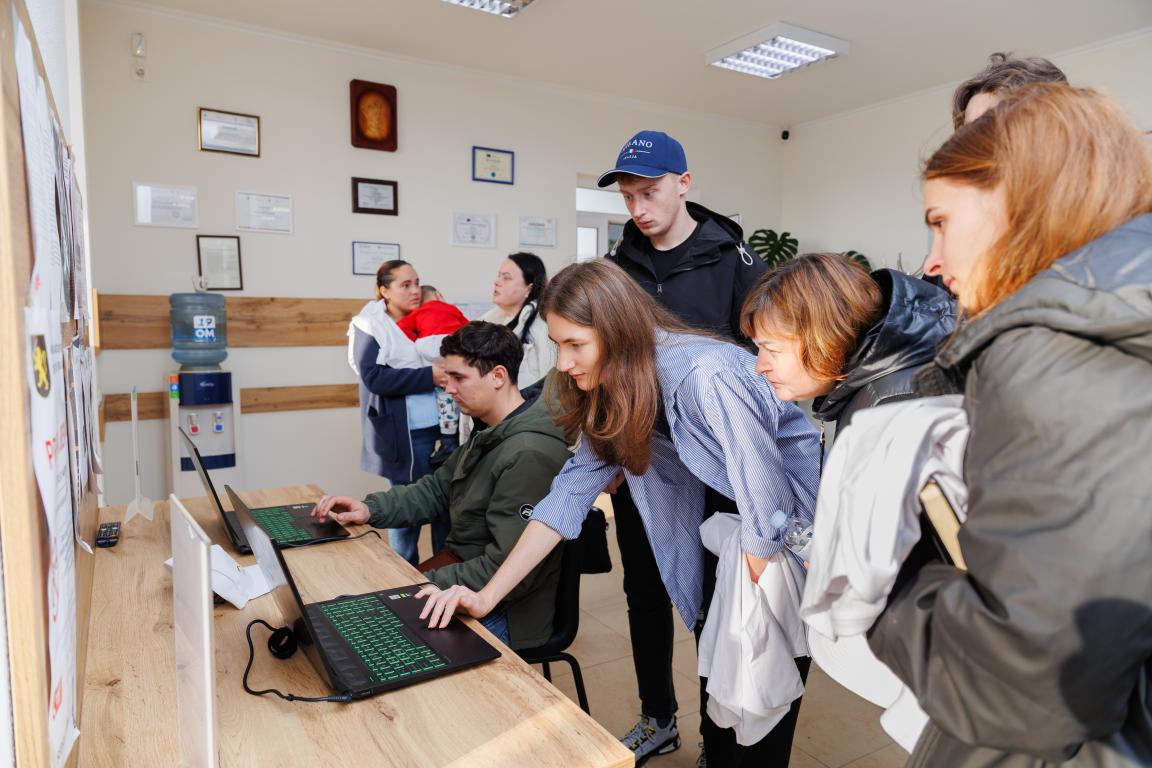 Residents of the village of Geamăna standing at a wooden table, using laptops in the newly established Unified Public Service Delivery Centre (CUPS).