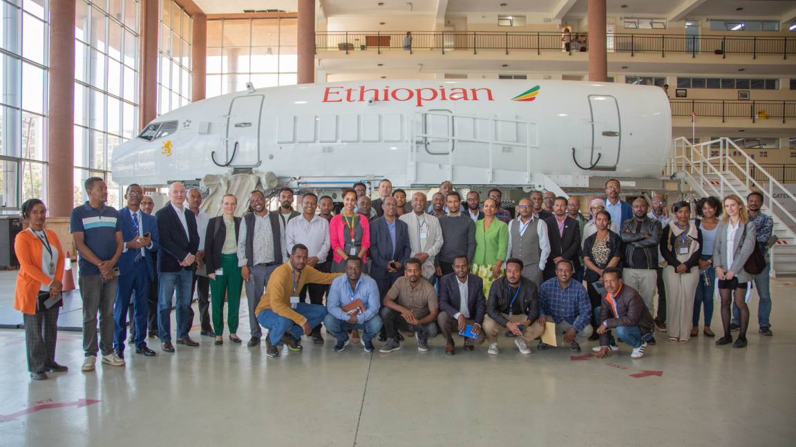 A large group of people poses for a group photo in front of part of an aeroplane at the Deep Dive Training event.
