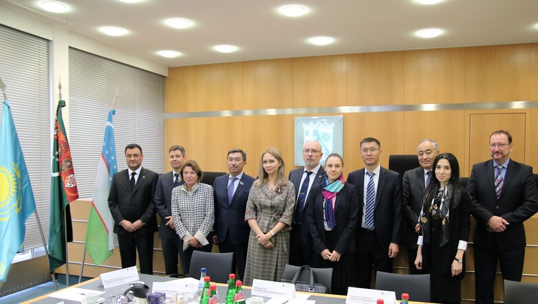 Eine zentralasiatische Delegation steht bei einem Besuch im Oberverwaltungsgericht Rheinland-Pfalz hinter einem Tisch zusammen.