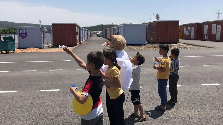 Kinder und eine Frau machen Seifenblasen in einer Containersiedlung.