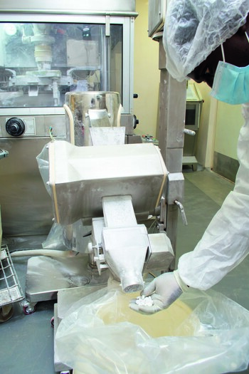 Ein Techniker in Schutzkleidung führt eine Kontrolle der Tabletten durch, die während der Herstellung aus der Maschine kommen.