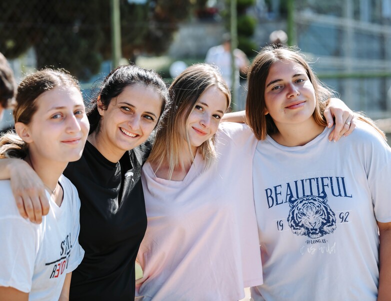 Vier Schülerinnen halten sich auf einem Sportplatz in den Armen und schauen lächeln in die Kamera. © GIZ / Nebojsa Petrevski