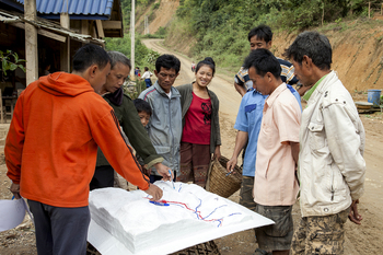 Eine Gruppe Laoten umringt ein Landschaftsmodell und bespricht die Landnutzungsplanung des Gebiets.