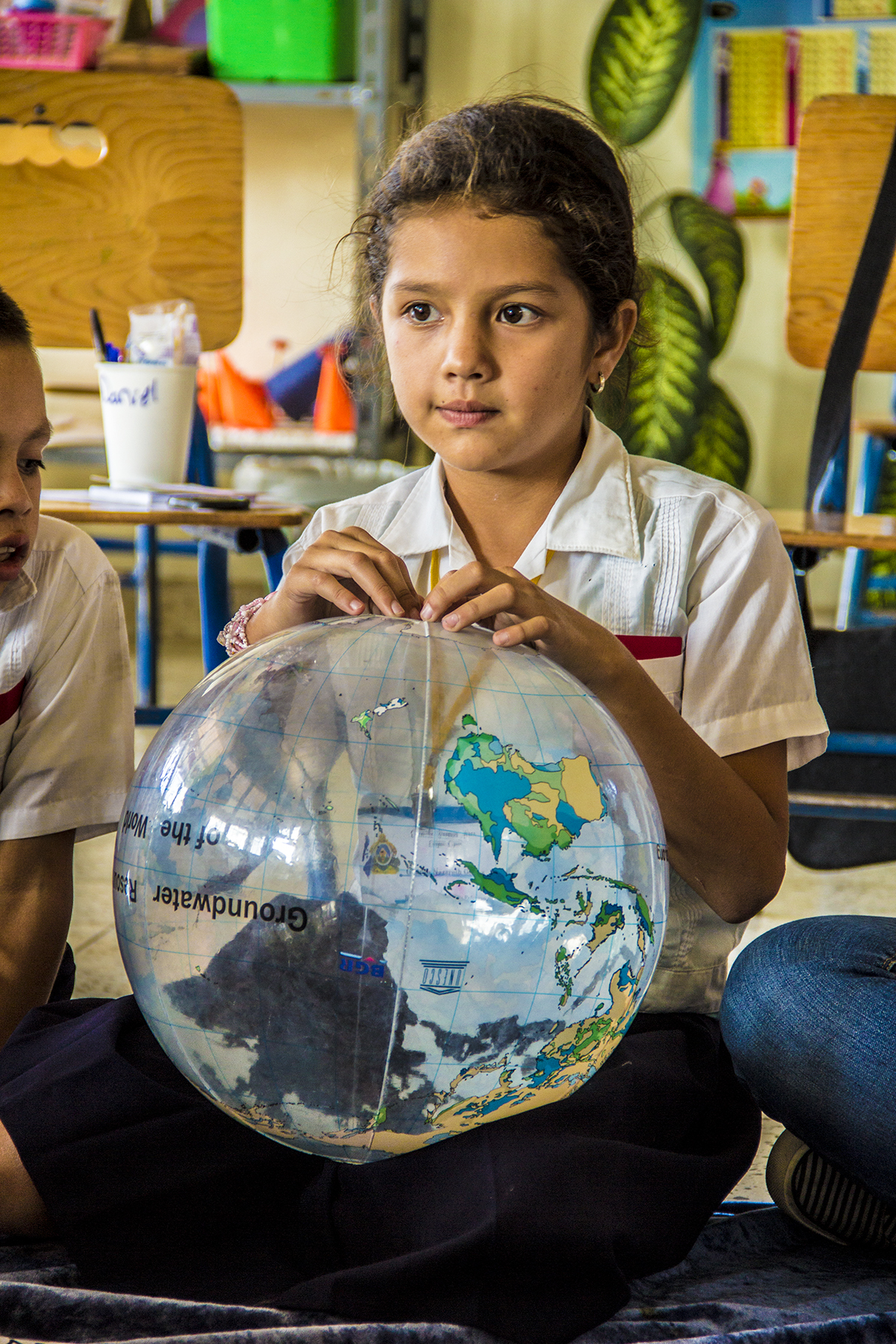 Eine Schülerin sitzt in einem Klassenraum und hält eine Weltkugel in ihrem Schoß.  ©GIZ/Felicitas Eser
