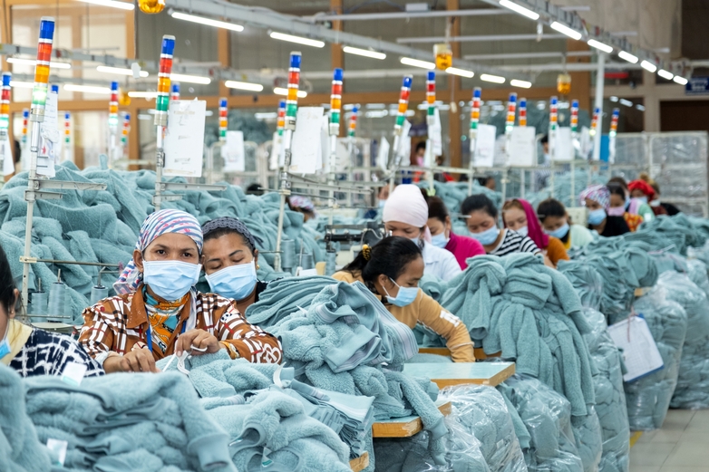 Arbeiterinnen in einer Produktionshalle fertigen Jacken an. © Roman König
