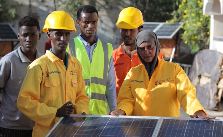 Fünf Menschen in Arbeitskleidung stehen hinter Solarpaneelen.