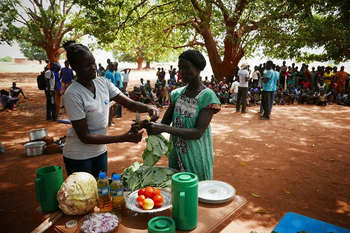 Eine Mitarbeiterin der NRO PAH zeigt einer Frauengruppe im KUAJENA CENTRE JUR RIVER COUNTY die Essenszubereitung. 