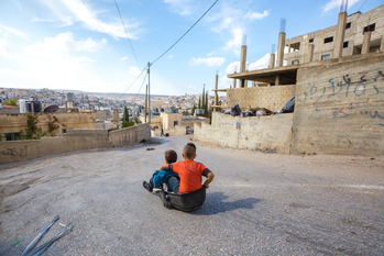 Zwei Jungen rutschen im Dehiesheh-Flüchtlingscamp mit einem Spielzeug den Hügel hinunter. © GIZ / Elias Halabi
