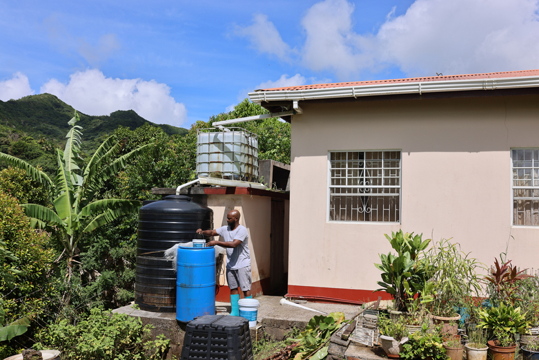 Ein Mann verwendet eine Regenauffanganlage neben seinem Wohnhaus. © GIZ Grenada / Arthur Daniel