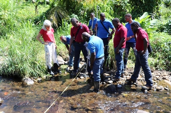 Mitarbeitende der nationalen Wasserbehörde stehen an einem Flussufer und messen den Wasserdurchfluss. © GIZ Grenada / Garwin Walters