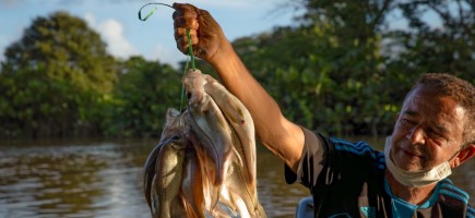 Ein Mann an einem Fluss hält gefangene Fische in der Hand.