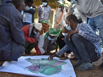 Personen stehen um eine Landkarte, ein Mann deutet auf eine Fläche.