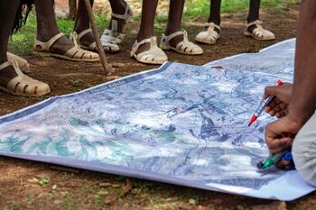 Eine Person malt etwas auf einer Landkarte ein, die zwischen Füßen auf dem Boden liegt.