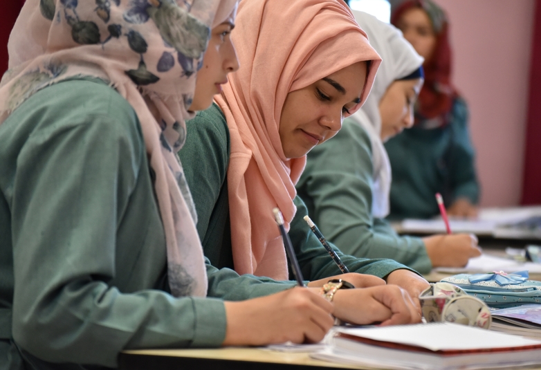 Syrische Schülerinnen sitzen hinter Tischen in einem Schulklassenraum und schreiben in Hefte. © GIZ/Cannizzo