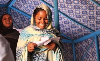 Eine junge Frau in traditioneller Kleidung hält ein Blatt Papier und lächelt.