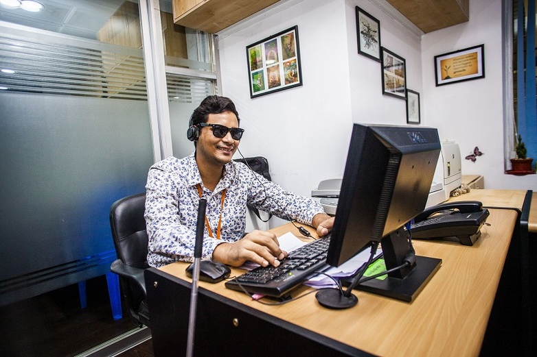 Ein Mann mit Sehbehinderung sitzt in Bangladesch am Computer, trägt Kopfhörer und lacht. Copyright: GIZ/ Fahad Abdullah Kaizer