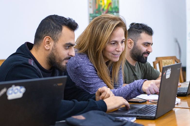 Zwei junge Männer und eine Frau sitzen an einem Tisch und schauen auf Laptops.