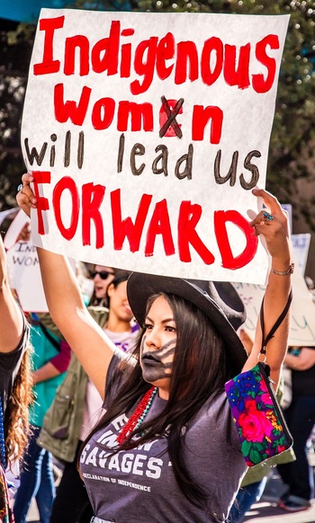 Eine indigene Frau hält ein Schild auf dem steht „Indigenous women will lead us forward“.