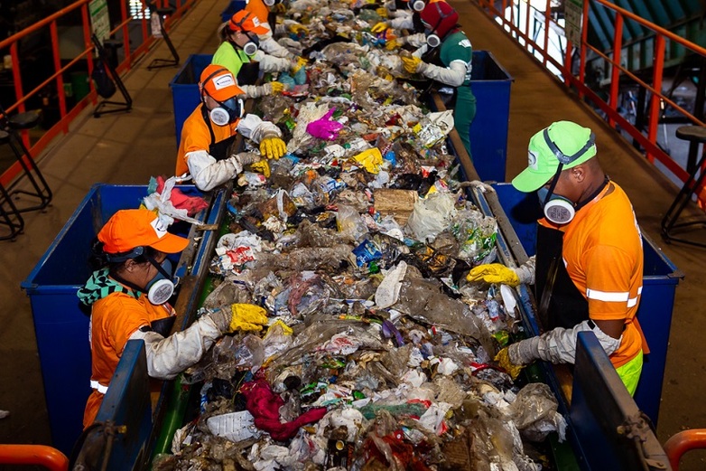 Mehrere Personen in Schutzkleidung sortieren Müll am Fließband.