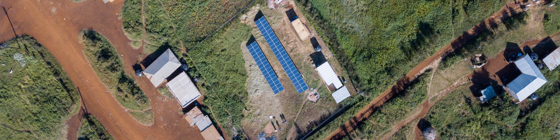 Eine Drohnenaufnahme zeigt eine Solaranlage zwischen vereinzelten Gebäuden in einer ländlichen Umgebung.