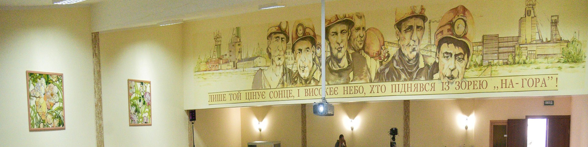 An die Wand eines Versammlungssaals ist eine gelbliche Malerei von Bergleuten vor einem Kohlebetrieb.