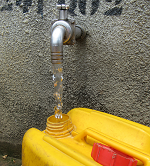 Yellow water canister with a running tap at a public standpipe. © GIZ