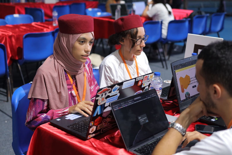 Junge Menschen sitzen bei einer Konferenz an ihren Laptops zusammen. 
