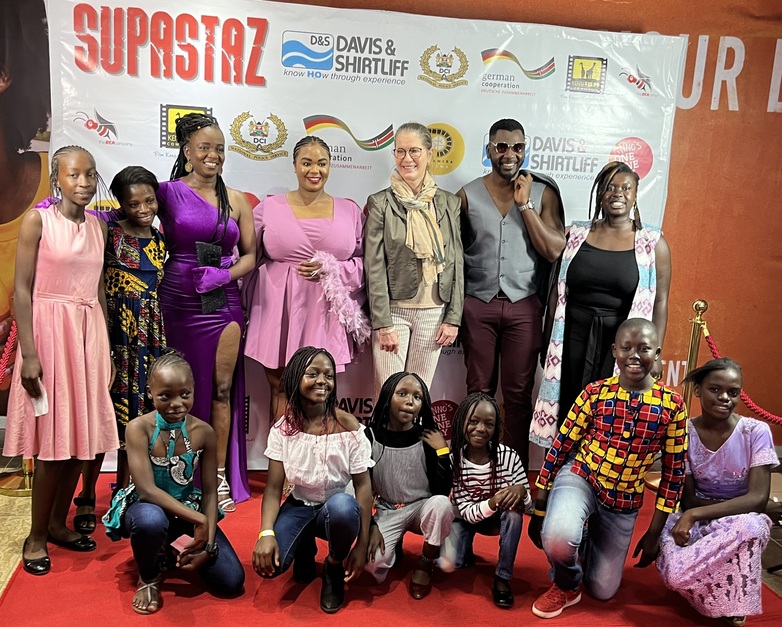Bei der Filmpremiere von „Supastaz“ steht eine Gruppe auf dem roten Teppich zusammen.